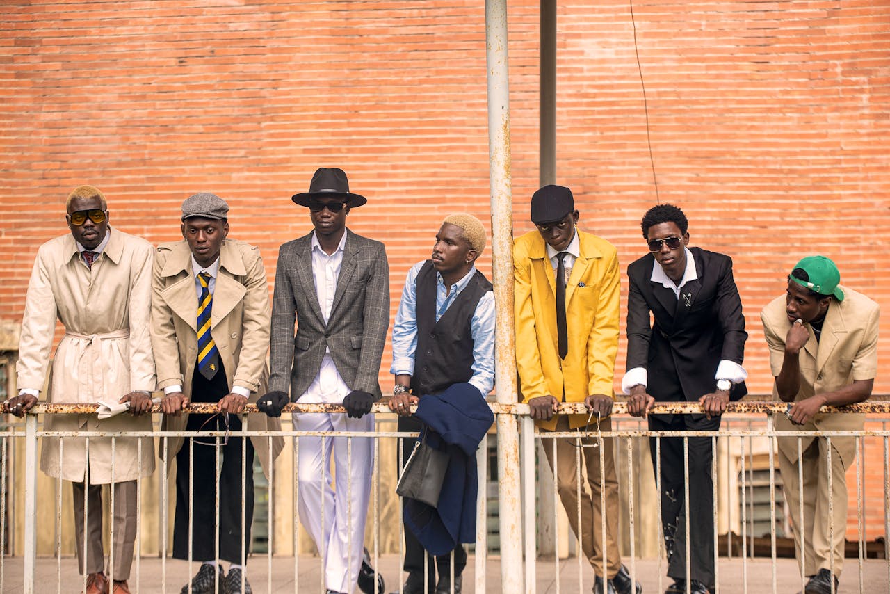 Seven men in vintage attire standing against a brick wall, exuding urban style.