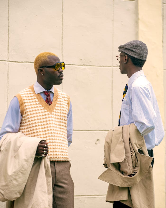 Two adults in retro outfits converse against a vintage urban backdrop, exuding cool style.