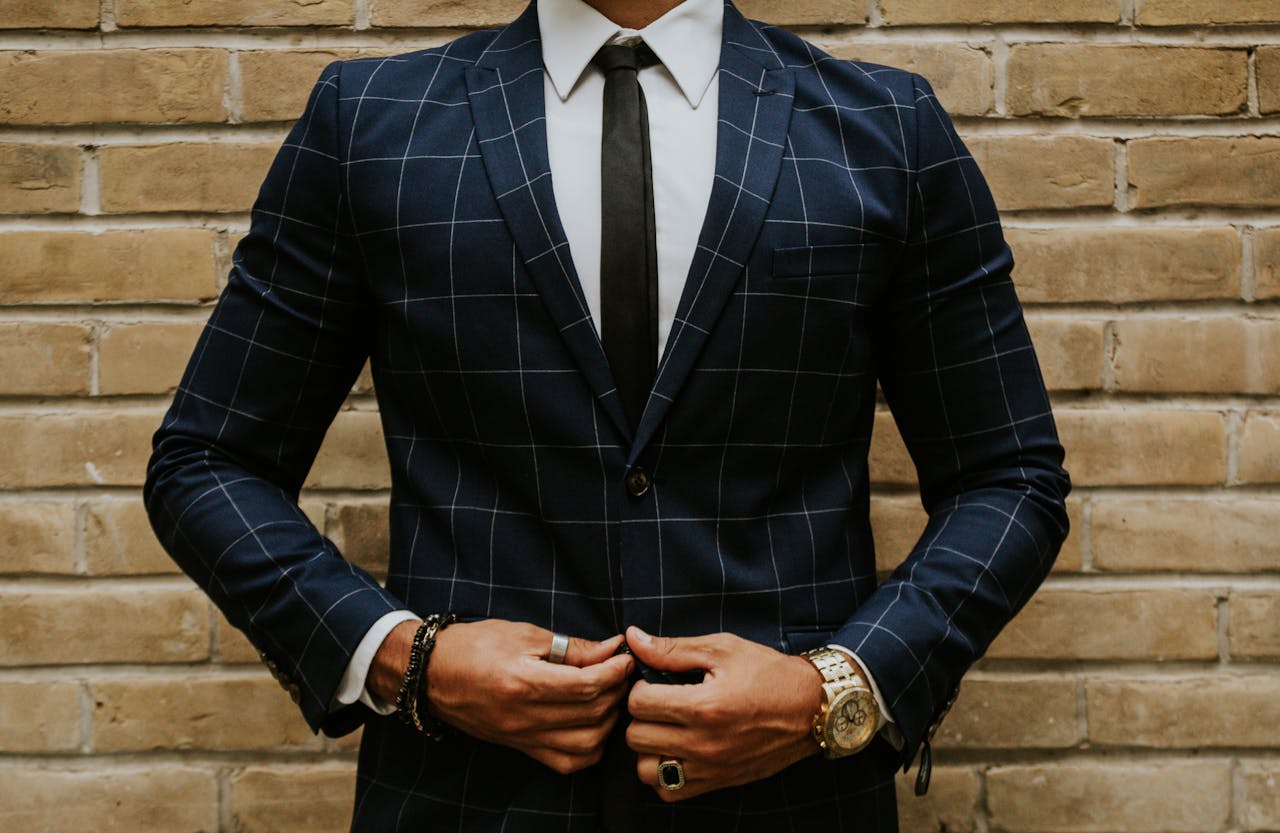 Crop anonymous businessman in white shirt with tie and dark ornamental jacket in rings on fingers standing near aged brick wall